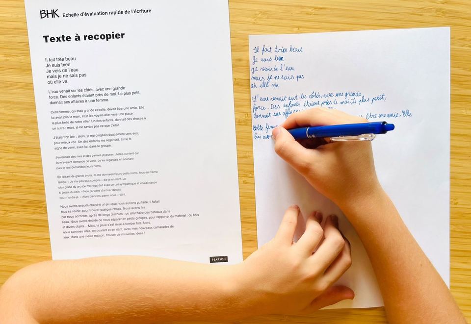 Enfant recopiant au stylo bleu le texte de l'échelle BHK posé à côté de sa feuille