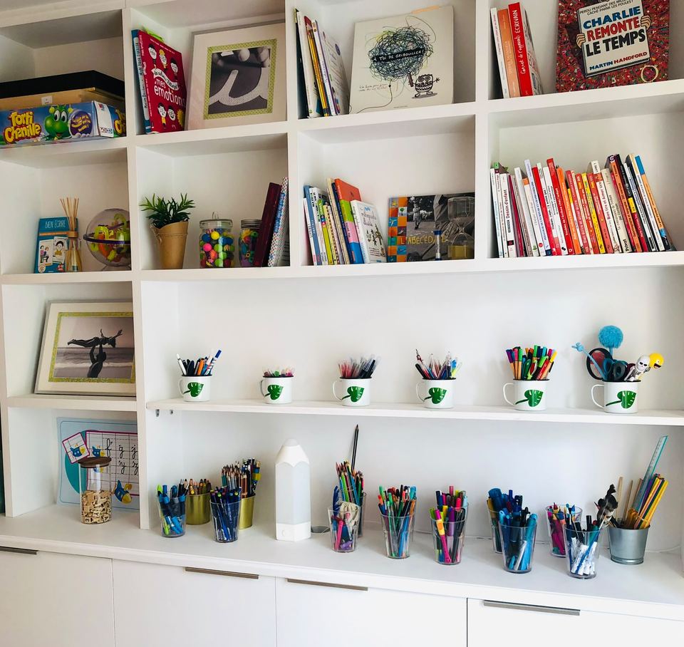 Étagères blanches garnies de livres, jeux et pots de crayons et feutres de couleur