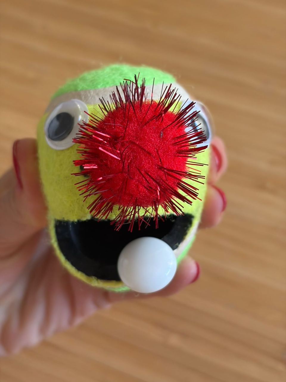 Balle de tennis transformée en personnage à la bouche ouverte, tenue dans une main