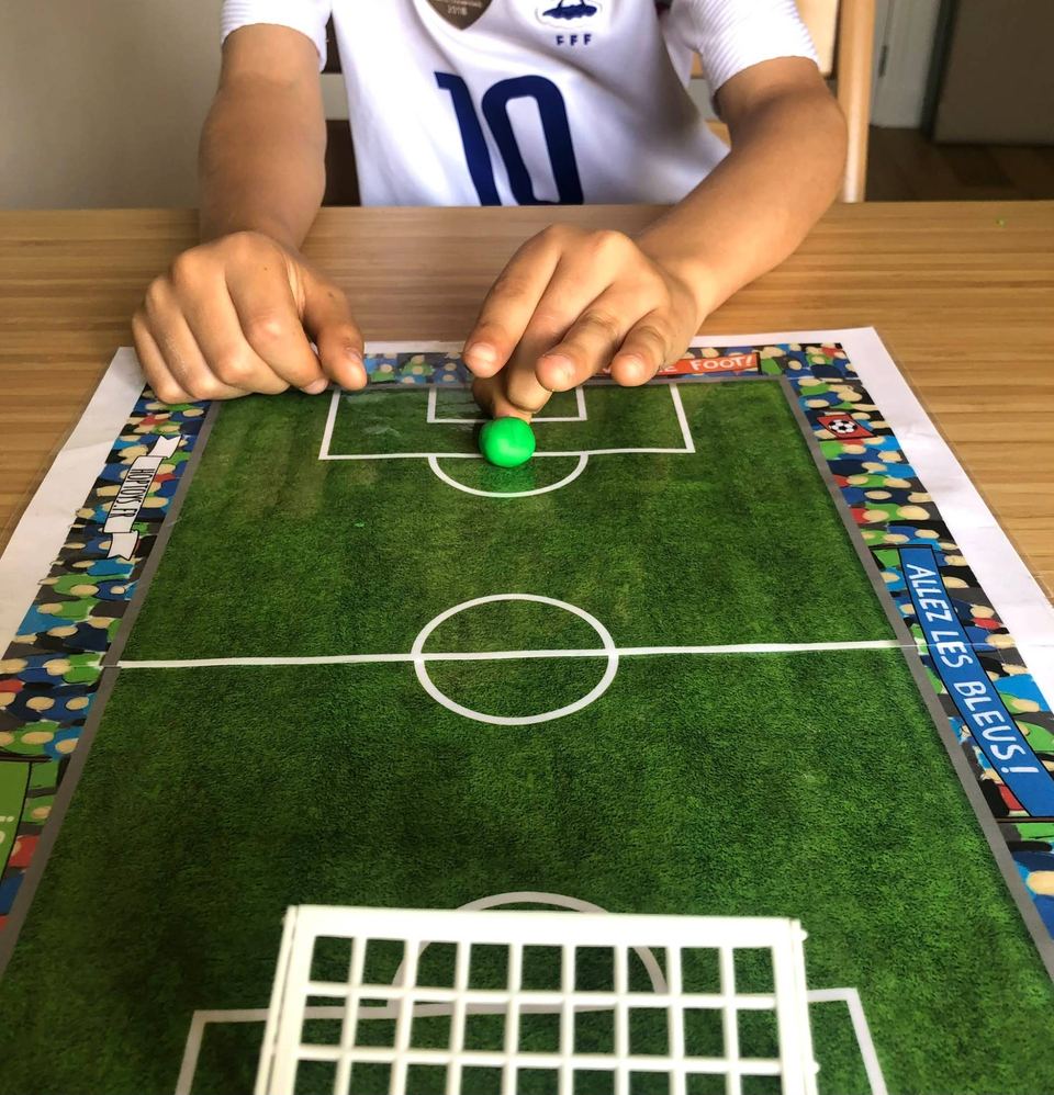 Enfant envoyant d'une pichenette une boule de pâte à modeler sur un terrain de football en papier