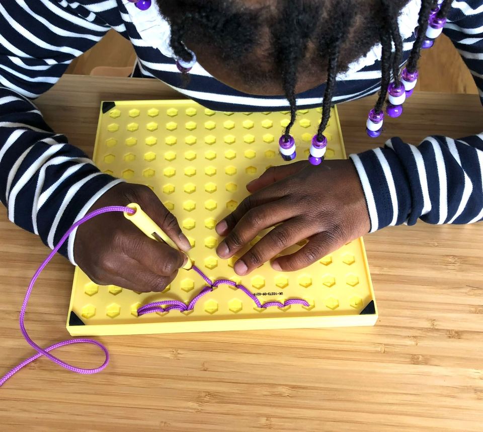 Enfant passant un lacet violet dans les trous d'une plaque jaune