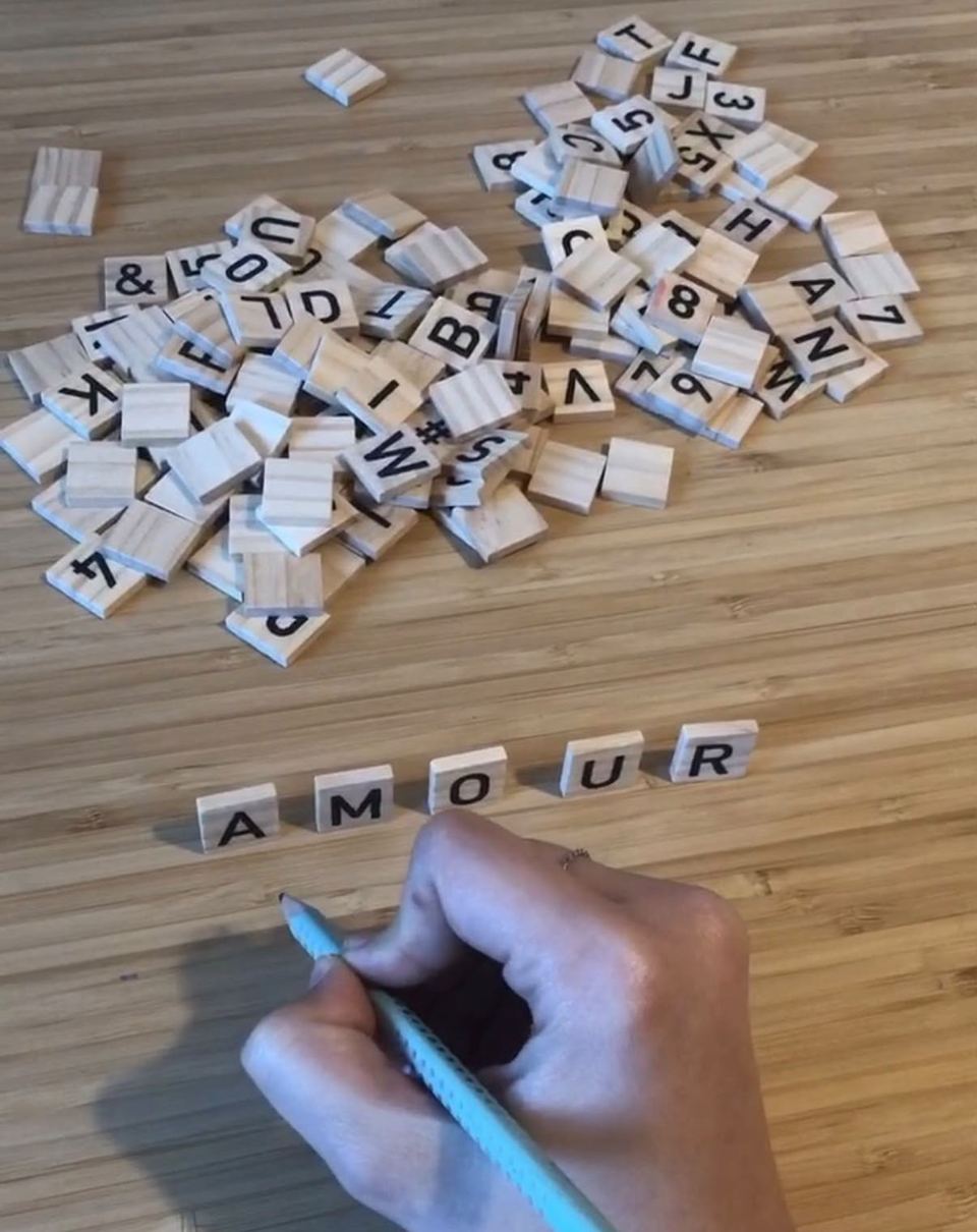 Main tenant un crayon devant le mot « AMOUR » formé avec des lettres en bois