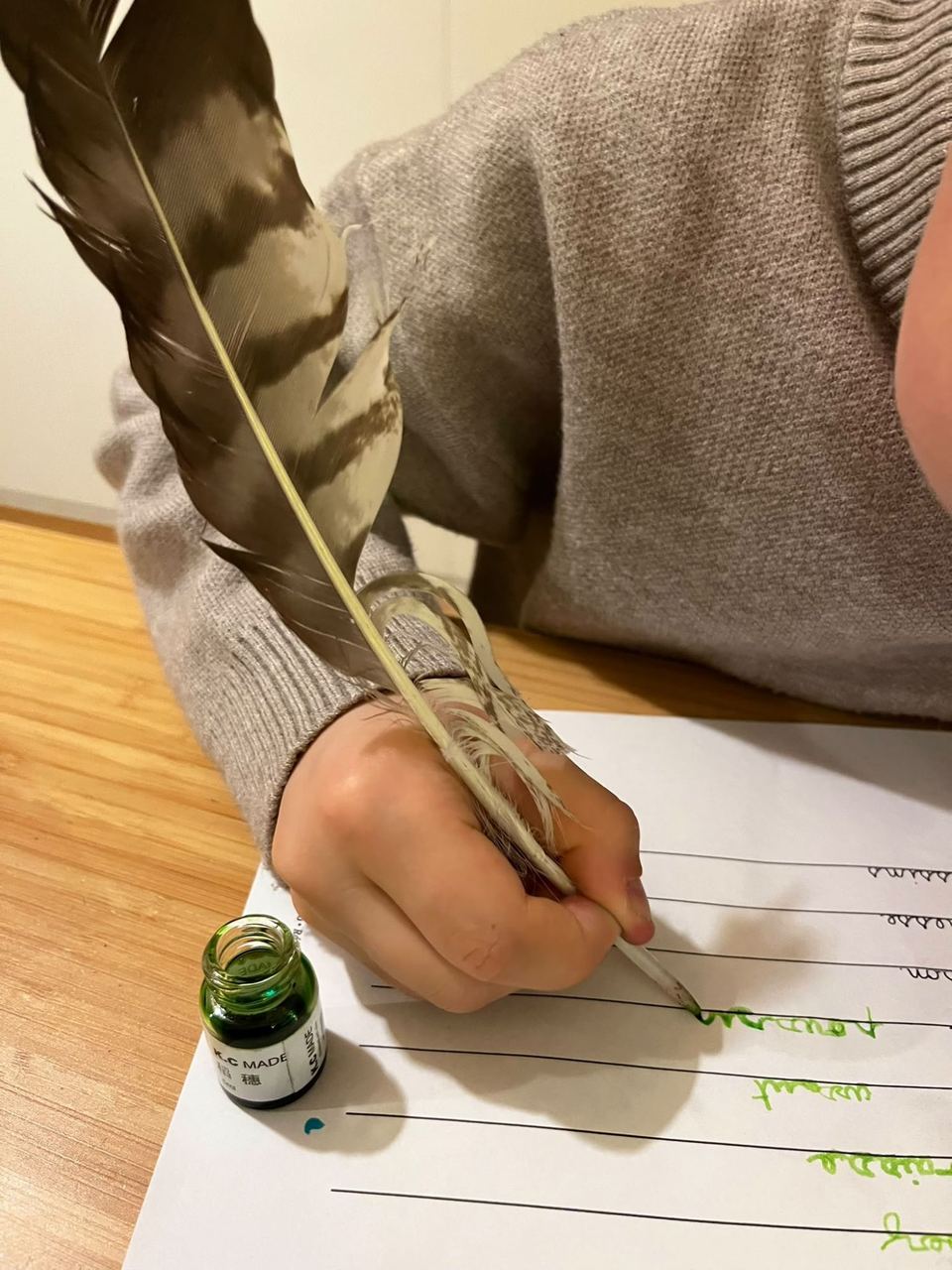 Enfant écrivant à la plume et à l'encre verte sur une feuille lignée