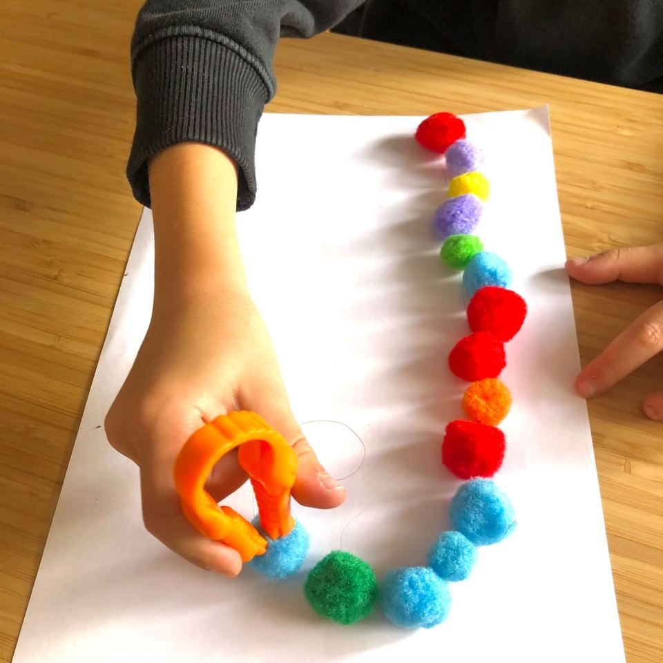 Main d'enfant utilisant une pince pour poser des pompons de couleur le long du tracé d'une lettre
