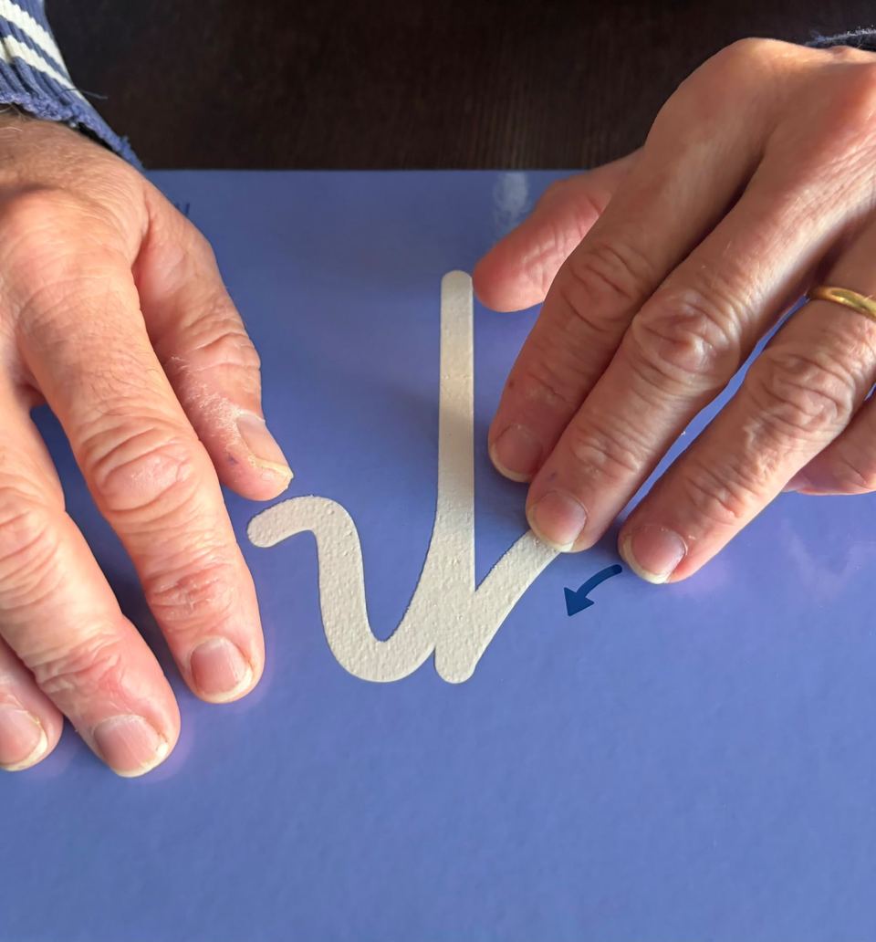 Mains d'adulte suivant du doigt le tracé d'une lettre cursive en relief