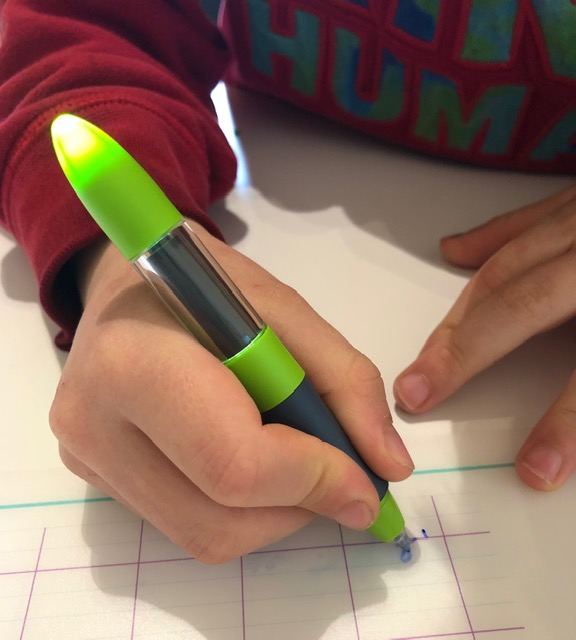 Enfant écrivant sur un cahier à grands carreaux avec un stylo dont l'extrémité s'allume en vert