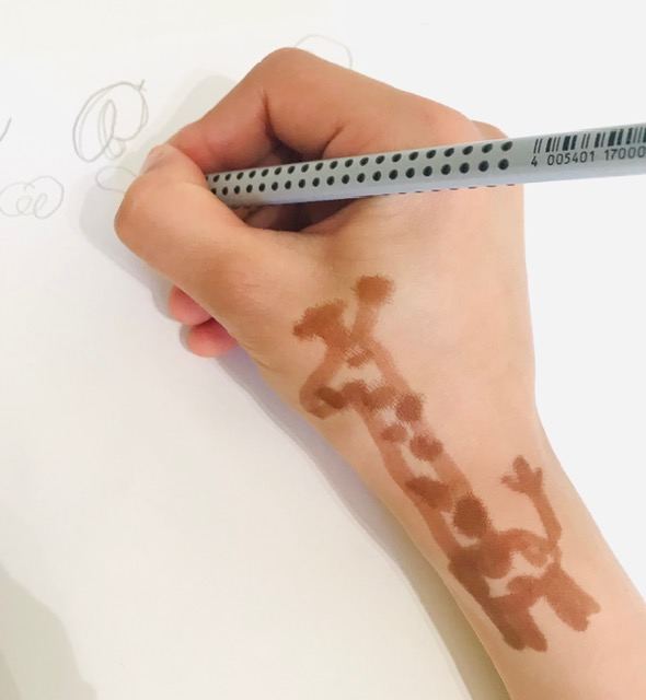 Main d'enfant tenant un crayon, avec une girafe dessinée le long du poignet pour guider sa position